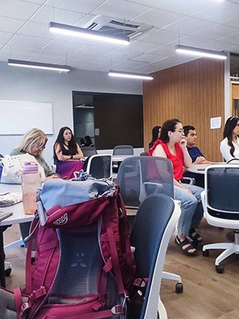 Una clase en un ambiente moderno con estudiantes sentados alrededor de mesas.