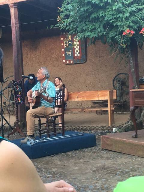 Un hombre toca la guitarra mientras una mujer lo acompaña en un escenario al aire libre.