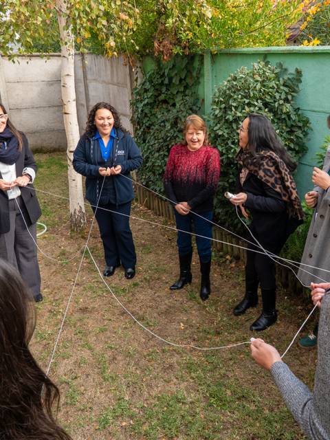 Un grupo de mujeres está participando en una actividad al aire libre, unidas por un hilo en el jardín.