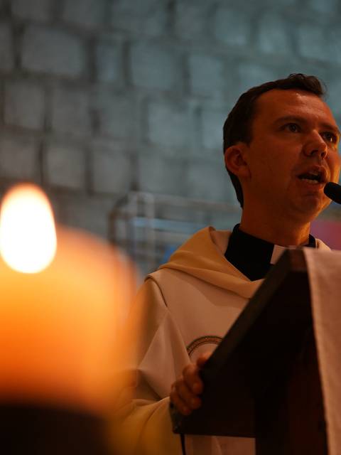 Un cura dando un sermón en una iglesia con una vela encendida en primer plano.