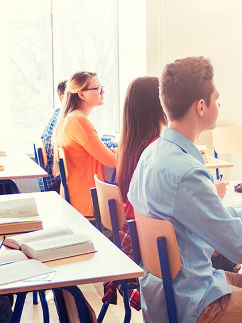 Un grupo de estudiantes escucha atentamente a un profesor en un aula iluminada.