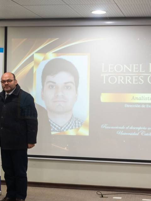 Dos hombres posando en un evento donde se entrega un reconocimiento en una presentación.