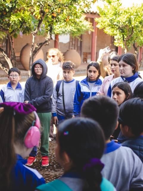 Un grupo de niños escucha atentamente a una adulta en un entorno al aire libre.