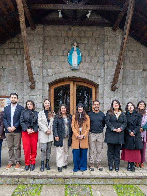 Un grupo de personas posando frente a una casa de piedra con una ventana grande.