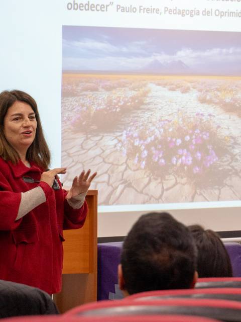 Una expositora presenta un tema inspirador frente a un auditorio atento y una proyección de paisaje detrás.