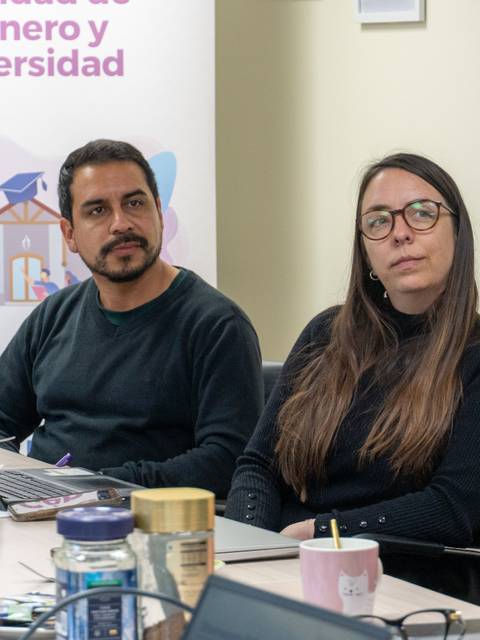 En la reunión, dos personas están escuchando atentamente mientras se discuten temas de género y diversidad.