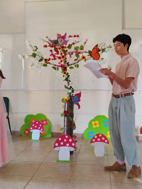 Un par de personas en un escenario decorado con un árbol de papel y setas de colores.