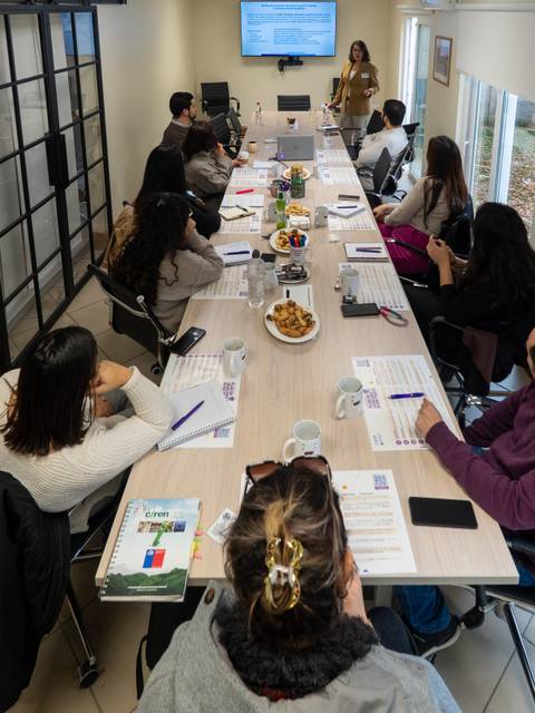 Una reunión empresarial en una sala amplia con participantes atentos y una presentadora en acción.