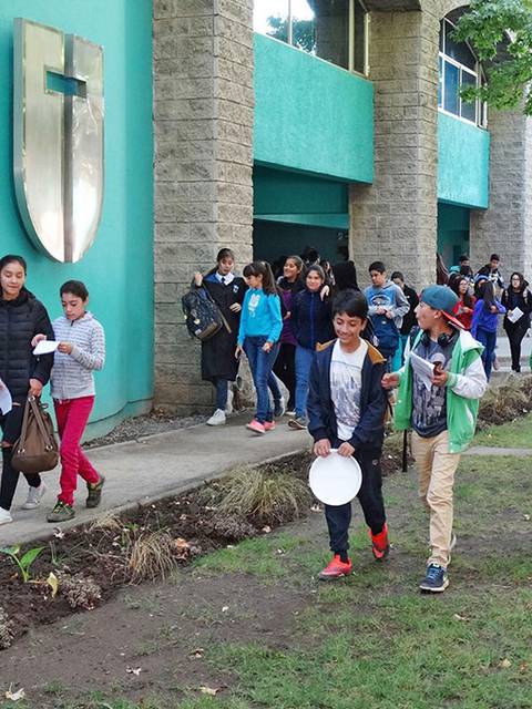 Un grupo de estudiantes camina por un pasillo escolar mientras llevan platos en las manos.