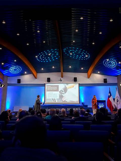 Una charla en un auditorio conpresentaciones en pantalla y público atento.