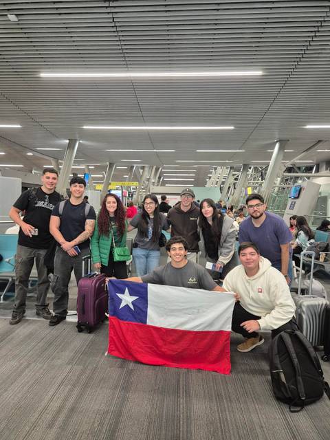Un grupo de amigos se reúne en el aeropuerto sosteniendo una bandera chilena.