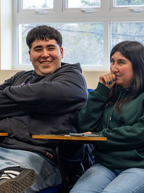 Dos estudiantes en una sala de clases compartiendo un momento de risa.