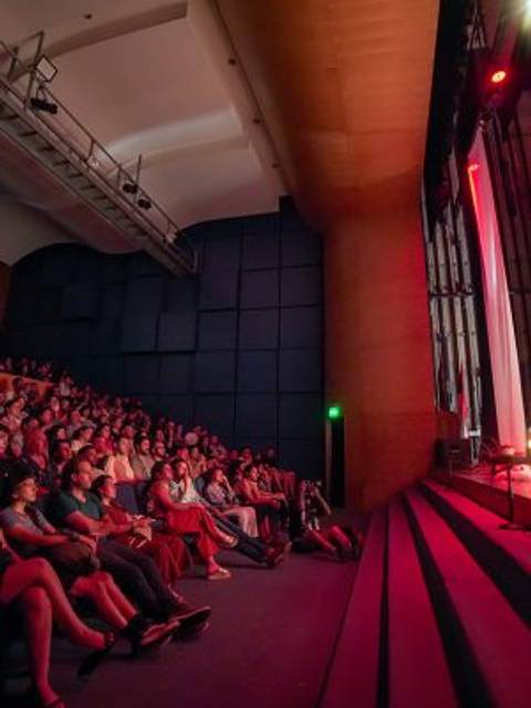 Una multitud observa atentamente en un auditorio iluminado durante un evento.