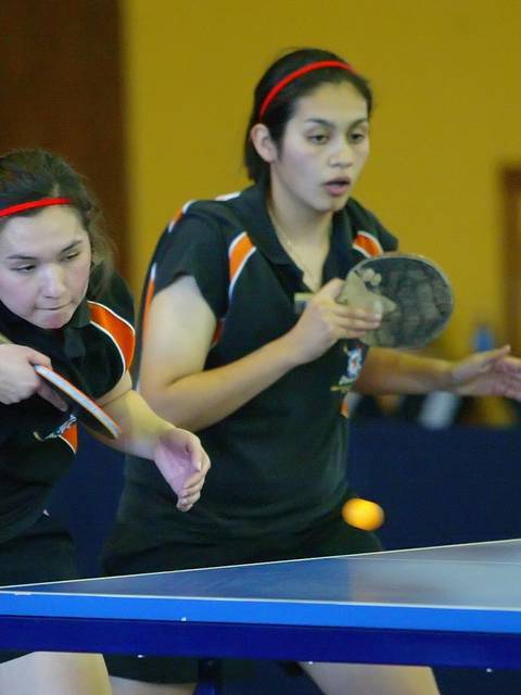 Dos jugadoras de tenis de mesa se preparan para golpear la pelota en un partido.