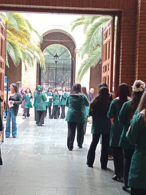 Un grupo de personas vestidas con chaquetas verdes se encuentra en un espacio amplio, esperando en un evento.