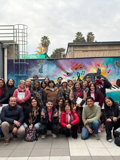 Un grupo grande de personas posando frente a un mural colorido en una plaza chilena.