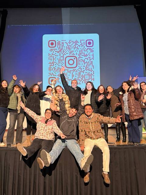 Un grupo de jóvenes en un escenario celebrando y posando alegremente frente a un código QR gigante.