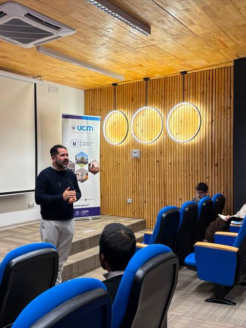 Un expositor presenta frente a un público en una sala moderna de conferencias.