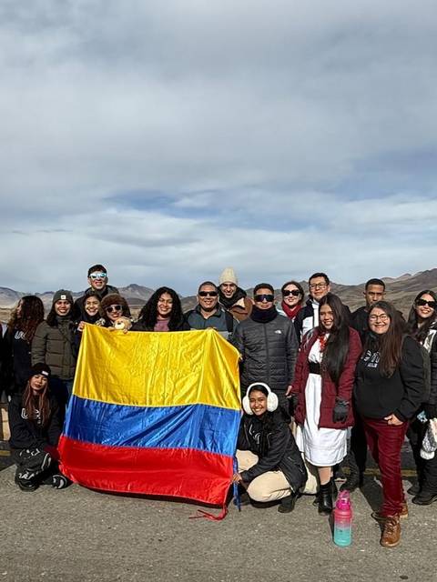 Un grupo de personas posando con banderas de Colombia y otra bandera, en un paisaje montañoso.