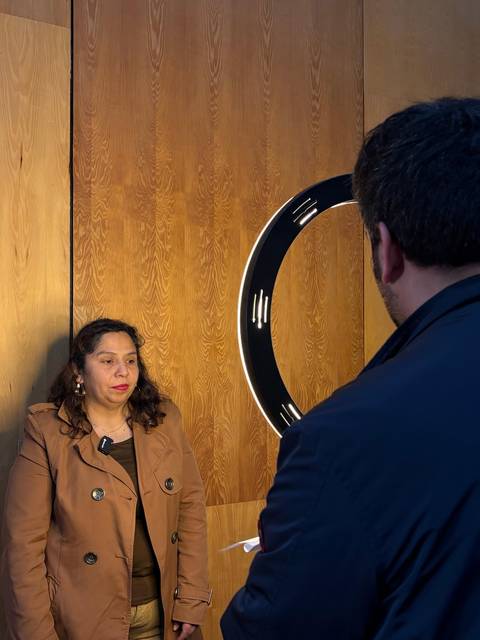 Una mujer posando frente a una luz circular mientras un hombre la observa.