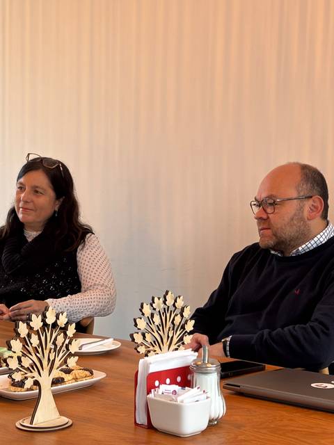 Dos personas conversando en una reunión con comida y bebida sobre la mesa.