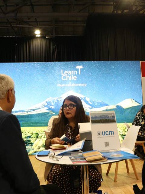 En el evento se observa a dos personas conversando en un stand de Learn Chile, con un fondo montañoso.