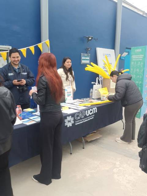 Una feria en la que se promocionan servicios educativos con varias personas interactuando en un stand.