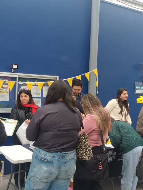 En un evento al aire libre en Chile, varias personas interactúan en un stand decorado con banderines amarillos.