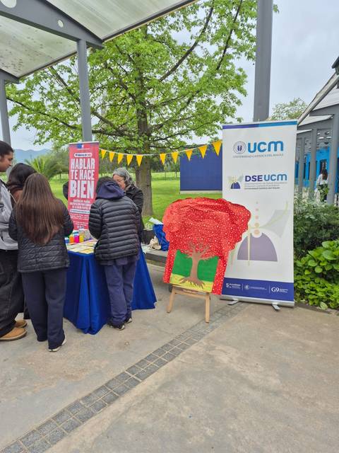 En la imagen se ve un evento al aire libre con personas interactuando en un stand y una colorida decoración al fondo.
