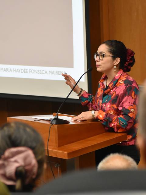 Una mujer vestida con una blusa colorida está dando una presentación en un evento.