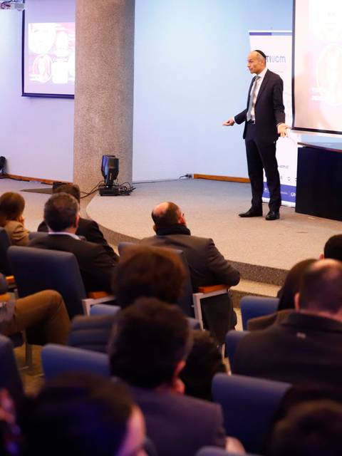 Un conferencista presenta ante un público atento en una sala iluminada.