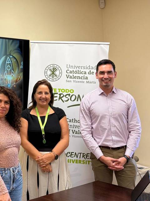 Tres personas posando frente a una presentación sobre el modelo de vinculación universitaria en un ambiente académico.