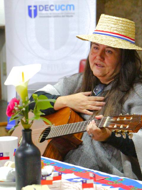 Una mujer vestida con un atuendo tradicional chileno toca la guitarra mientras celebra con un ambiente festivo.