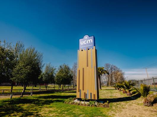 Un letrero moderno de la Universidad Católica del Maule en un entorno de naturaleza.
