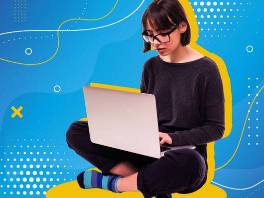 Una persona sentada en el suelo usando una computadora portátil con un fondo colorido.