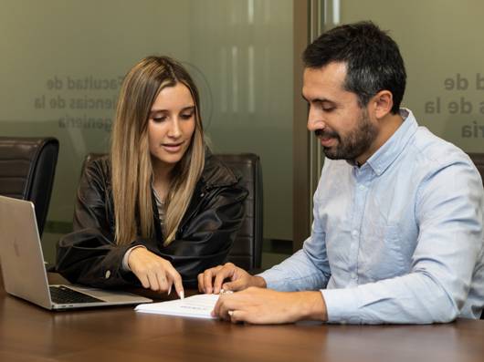Una pareja de profesionales discutiendo documentos frente a una laptop en una oficina.