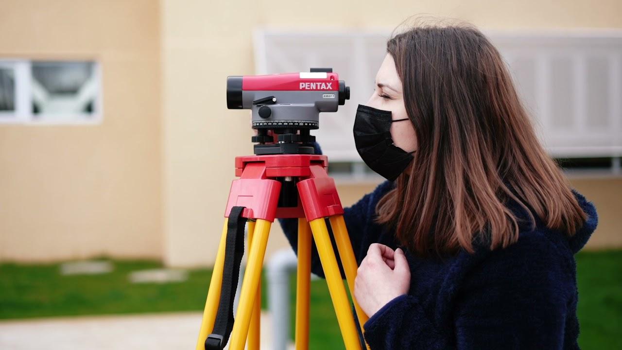 Una mujer con mascarilla observa a través de un nivel óptico en un trípode.