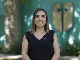 Una mujer sonriente con cabellera larga y suelta, vestida de negro, posa frente a un fondo colorido.