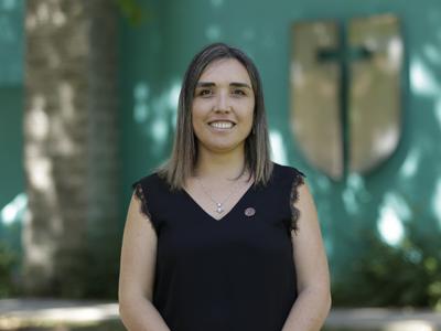 Una mujer sonriente con cabellera larga y suelta, vestida de negro, posa frente a un fondo colorido.