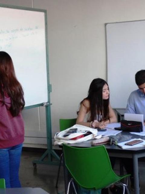 Un grupo de estudiantes trabaja en un aula, algunos escriben en una pizarra y otros colaboran en una mesa.