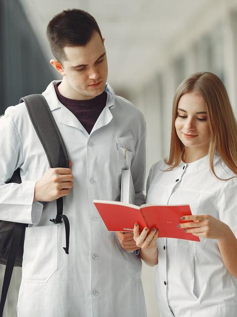 Dos jóvenes en un ambiente clínico revisan un libro juntos.