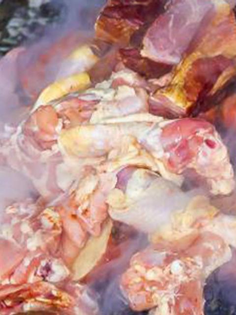 Una gran cantidad de carne se encuentra apilada, mientras se produce humo alrededor.