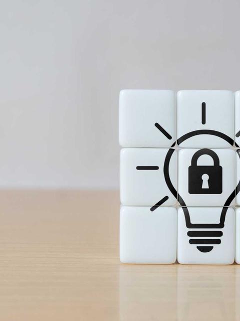 Un cubo de puzzle blanco con una bombilla y un candado dibujados en el centro, simbolizando ideas protegidas.