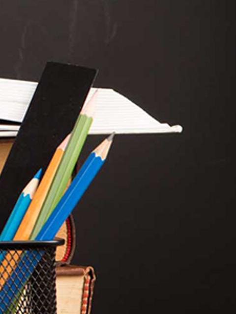 Una pila de libros con un cuaderno abierto y lápices de colores listos para anotar.