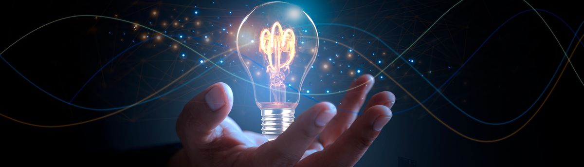 Una mano sostiene una bombilla encendida en un fondo oscuro, simbolizando ideas y creatividad.