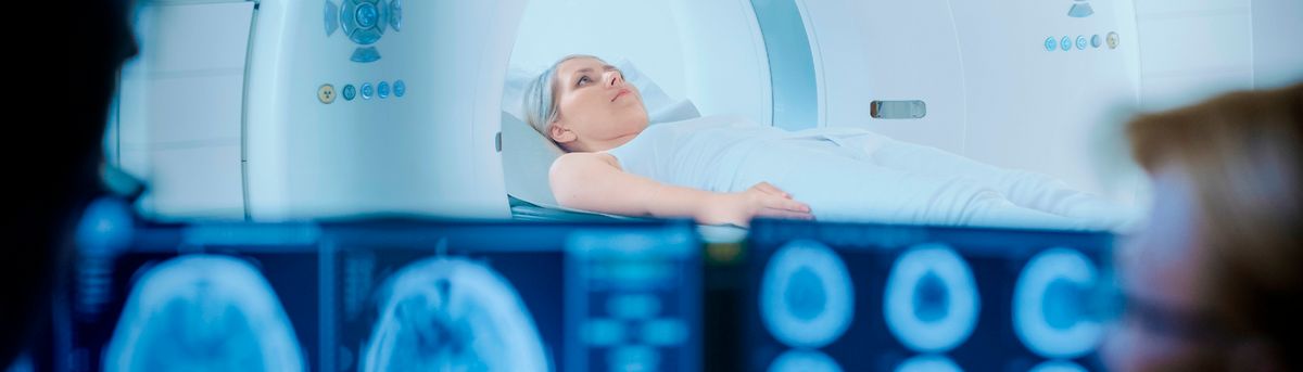 Una persona se encuentra acostada en una máquina de resonancia magnética mientras observa pantallas con imágenes médicas.