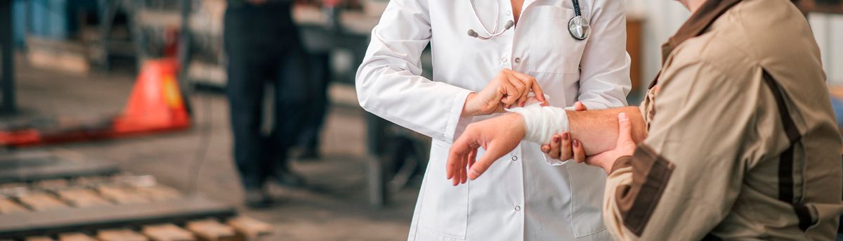 Una doctora atiende una herida en la muñeca de un paciente en un entorno industrial.