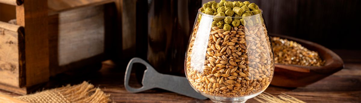 Un vaso de vidrio contiene granos de cebada y lúpulo sobre una mesa de madera.