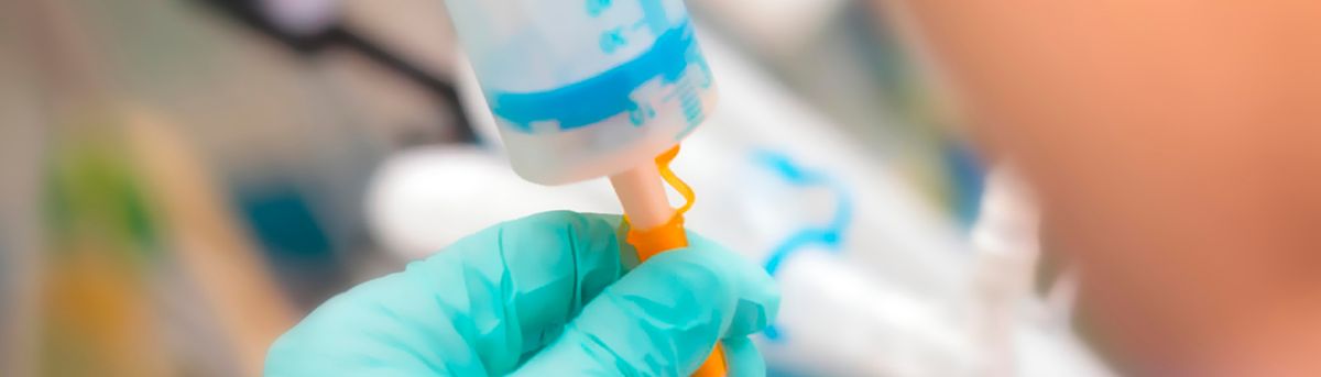 Una mano con guante sostiene un dispositivo médico que parece ser un conector de tubos.