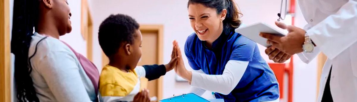 Una enfermera sonriente interactúa con un niño en un entorno médico, mientras una mujer lo observa.